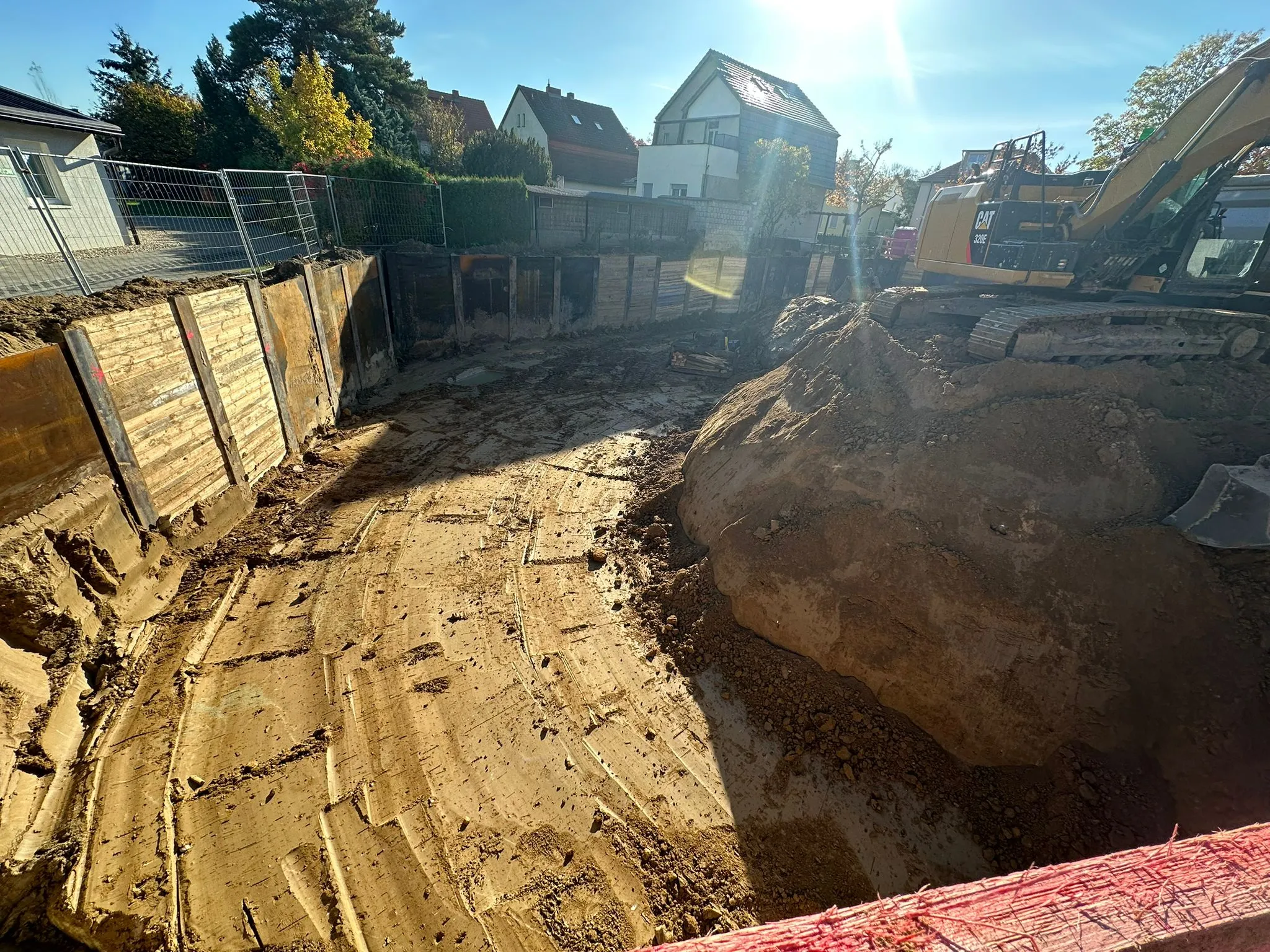 Berliner Verbau einer Cavator-Baustelle: Trägerbohlwand mit pinkfarbener Perimeterdämmung und CAT-Bagger